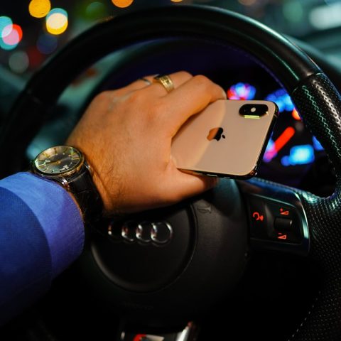 person holding gold iPhone Xs while driving black Audi vehicle